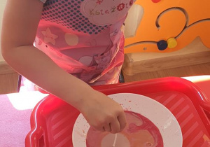 Nikola za pomocą patyczka i płynu do mycia naczyń tworzy magię kolorów.